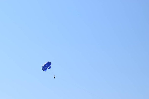 Parakting rekreacyjny tło - sylwetka trzech osób pod niebieskim baldachimem spadochronowym holowane za łodzią. Parasailing trio na niebie nad Morzem Śródziemnym. - Zdjęcie, obraz