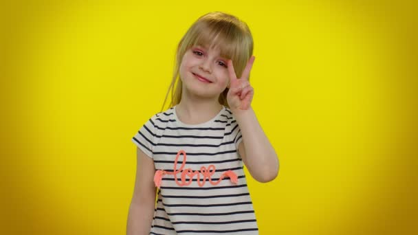 Lustiges blondes lächelndes Kind zeigt Siegeszeichen in der Hoffnung auf Erfolg und Sieg und macht Friedensgeste - Filmmaterial, Video