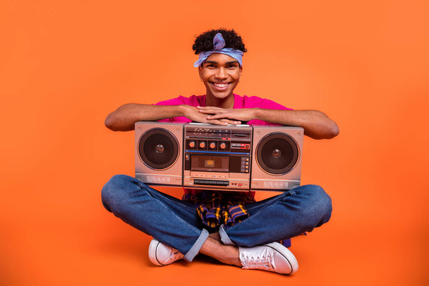 Full length body size photo of young man with sitting keeping boom box smiling isolated vivid orange color background - Foto, Bild