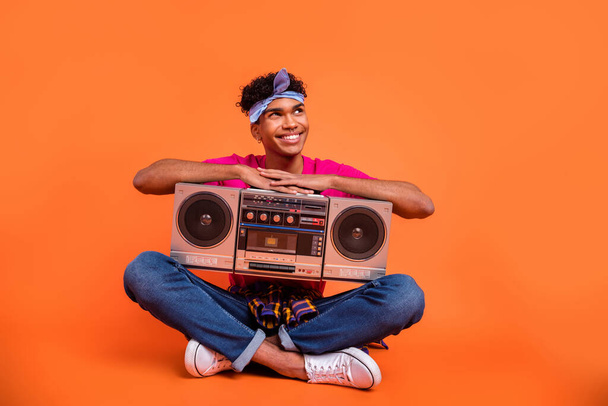Full length body size photo of curious dreamy guy with tape recorder looking empty space isolated vibrant orange color background - Фото, зображення