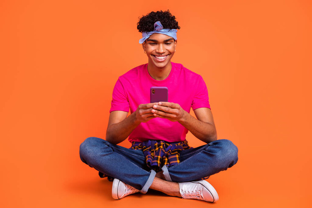 Full length body size photo of young hipster browsing internet with smartphone smiling isolated bright orange color background - Photo, image
