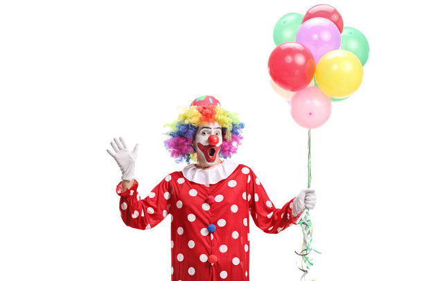 Clown holding a bunch of balloons and waving at camera isolated on white background - Photo, Image