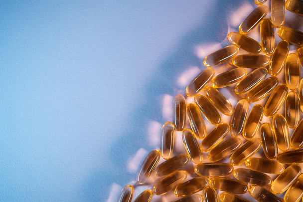 handful of golden fish oil capsules omega 3 vitamins on purple background - Фото, изображение