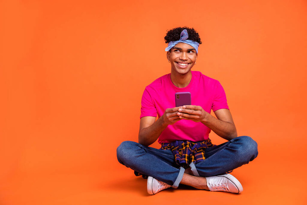 Full length body size photo of curious dreamy hipster reading news with mobile phone isolated vivid orange color background copyspace - Photo, image