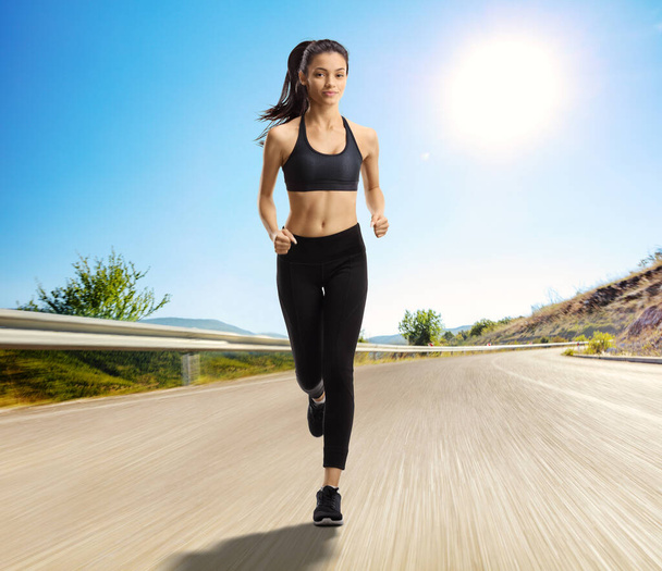 Full length portrait of a mixed race female running towards the camera on an open asphalt road - Photo, Image