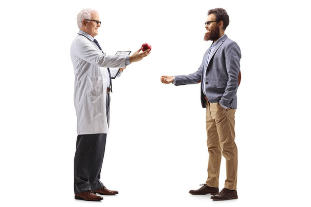 Full length profile shot of a male doctor giving an apple to a bearded man isolated on a white background - Foto, imagen