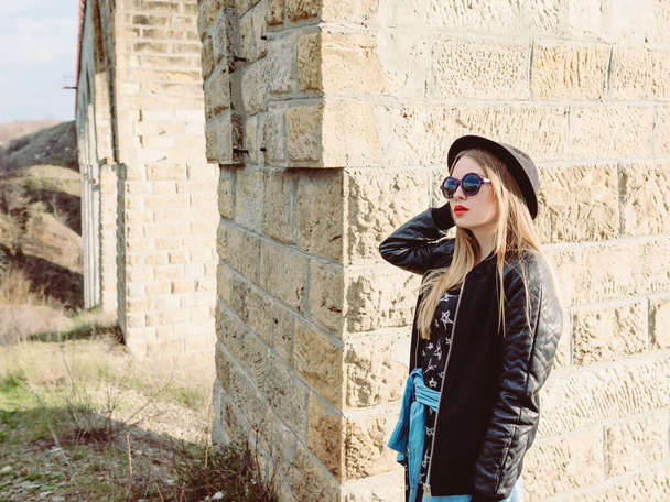 Stylový hipster žena cestovatel v slunečních brýlích a černý klobouk u starého mostu viaduktu. Cestování, Evropa, móda, styl koncepce - Fotografie, Obrázek