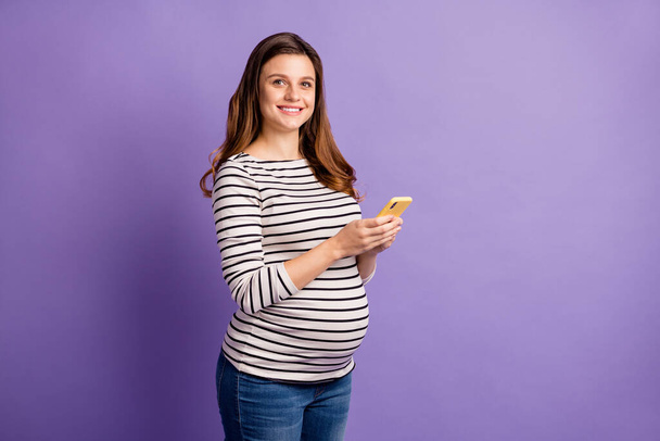 Photo of pregnant lady hold telephone look camera wear striped shirt isolated violet color background - Fotó, kép
