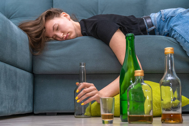 Cansada jovem mulher de cabelos escuros deitada no sofá após uma festa em casa close-up, ao lado de garrafas vazias no chão - Foto, Imagem