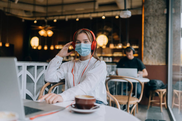 Ein Mädchen sitzt mit Kopfhörern in einem Café. Coronavirus-Ausbruch. - Foto, Bild