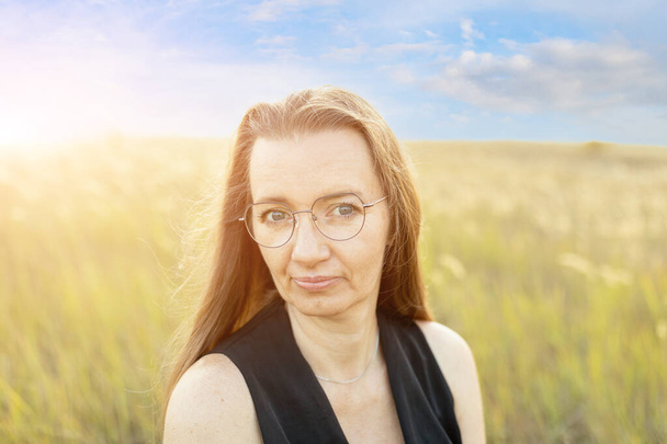 Gros plan d'une femme adulte aux cheveux longs dans un champ au coucher du soleil - Photo, image