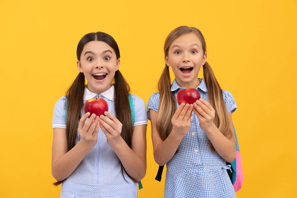 Surprised school age kis hold tasty organic vitamin apples yellow background, healthy food. - Фото, изображение