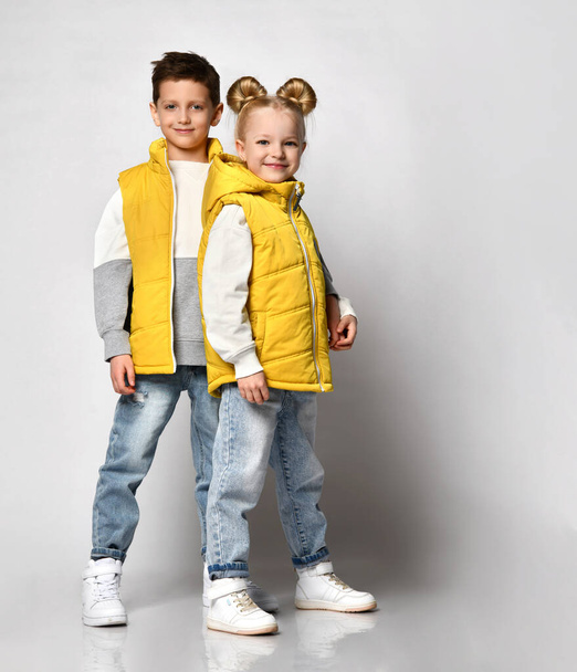 teenage boy and a girl walk holding hands in a yellow tank top, sleeveless zippered down jacket and jeans. - Foto, Imagem