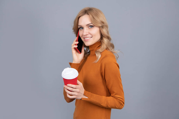 Happy girl parlare sul telefono cellulare in possesso di una tazza calda di tè o caffè bere sfondo grigio, pausa. - Foto, immagini