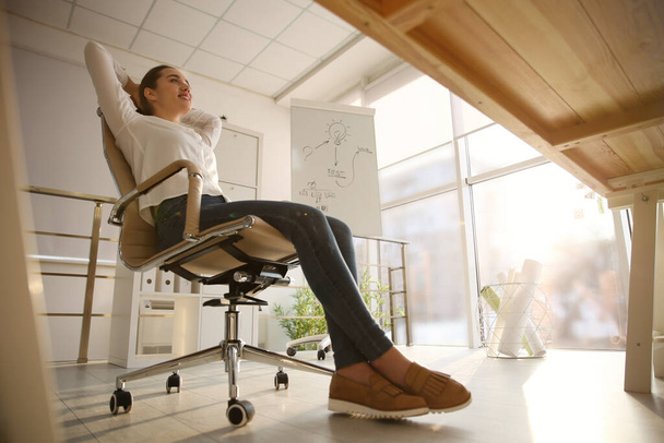 Young woman relaxing in office chair at workplace, low angle view - Φωτογραφία, εικόνα