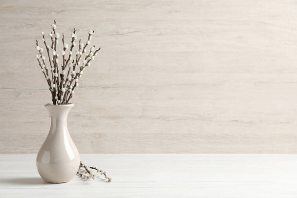 Beautiful pussy willow branches in vase on white wooden table, space for text - Foto, imagen