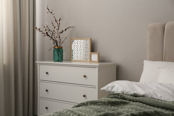 Flowering tree twigs and decor on white chest of drawers in bedroom - Fotografie, Obrázek