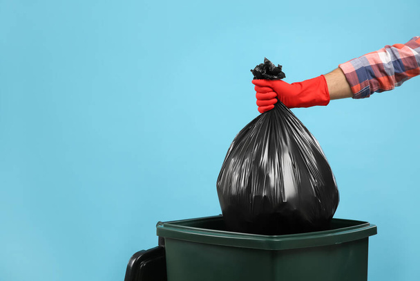 Man throwing garbage bag into bin on light blue background, closeup. Space for text - Foto, afbeelding