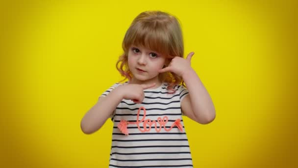 Little cute blondynka dziecko dziewczyna patrząc w aparat robi telefon gest jak mówi hej oddzwoń do mnie - Materiał filmowy, wideo