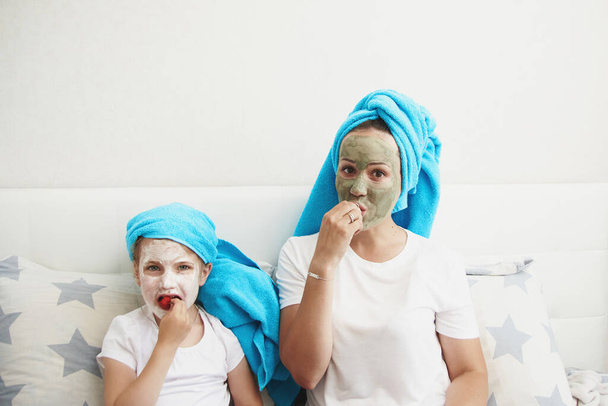 Morning care routine. Mom and daughter conduct beauty treatments. They are sitting on the couch and applying pieces of cucumber to their eyes. - Photo, Image
