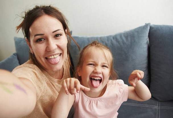 Young mother with her baby daughter take selfies and fool around looking at the camera - Photo, image