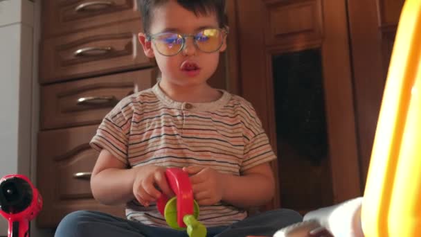 ragazzo caucasico con gli occhiali sta giocando con i giocattoli a casa sul pavimento - Filmati, video