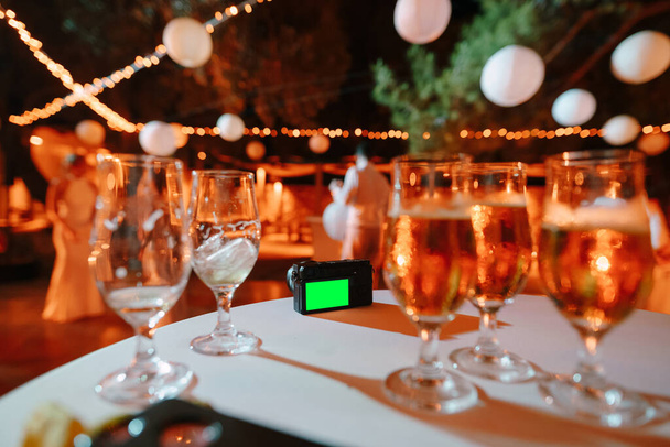 黒のデジタルカメラは、飲み物とガラスの背景に白いテーブルクロスで覆われたテーブルの上に立つ - 写真・画像