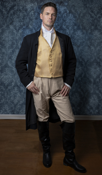 Komea Regency mies yllään kulta liivi, housut, ja musta takki ja seisoo huoneessa sininen tapetti ja puulattia.  - Valokuva, kuva