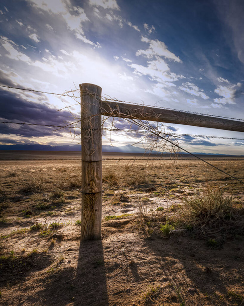 Ferme rurale à la campagne avec une clôture en fil de fer barbelé au coucher du soleil. Il ya des nuages dans le ciel. Le décor semble sec comme s'il y avait une sécheresse. - Photo, image