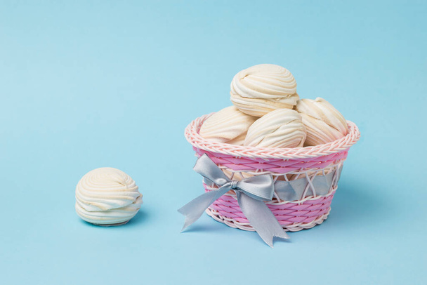 Proutěný koš s vanilkovým meringue na modrém pozadí. Lahodná sladkost vajec a cukru. - Fotografie, Obrázek