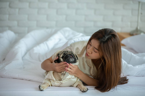 Beautiful Asian young woman playing with her cute dog pug breed in cozy bedroom at home happiness and cheerful - Fotoğraf, Görsel