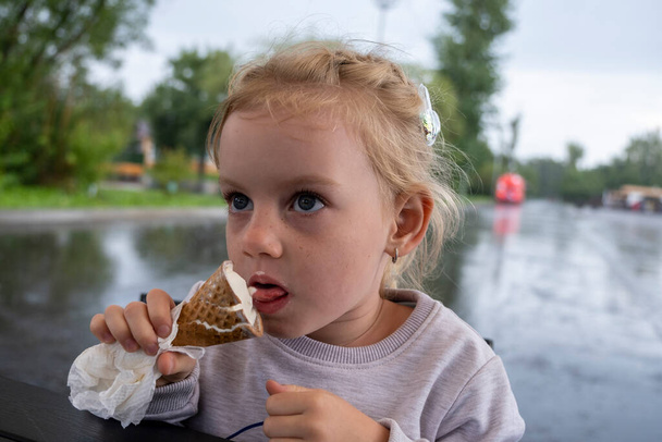 Chica comiendo helado en un café al aire libre en un día lluvioso - Foto, Imagen