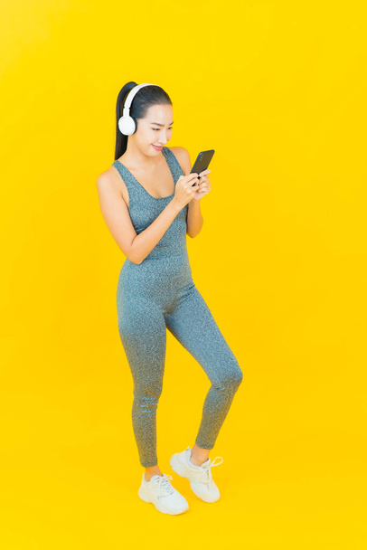 Ritratto bella giovane donna asiatica indossare abbigliamento sportivo e telefono per ascoltare musica con cuffie su sfondo giallo - Foto, immagini