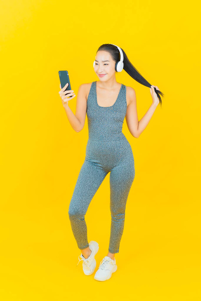 Portret piękna młoda azjatycka kobieta nosić odzież sportową i telefon do słuchania muzyki ze słuchawką na żółtym tle - Zdjęcie, obraz