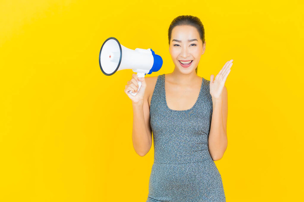 Portrait beautiful young asian woman with sportswear and megaphone on yellow background - Photo, Image