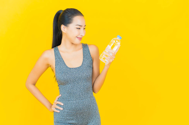Portrét krásná mladá asijská žena se sportovním oblečením a láhev vody na žlutém pozadí - Fotografie, Obrázek