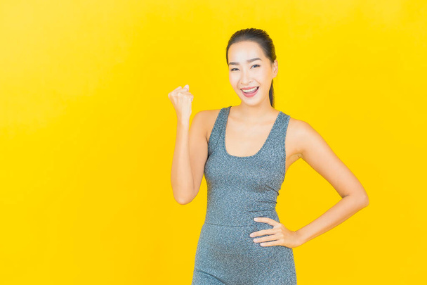 Портрет красивая молодая азиатка в спортивной одежде, готовая к упражнениям на желтом фоне - Фото, изображение