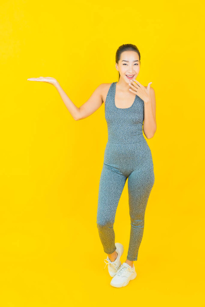Portret mooie jonge aziatische vrouw met sportkleding klaar voor oefening op gele achtergrond - Foto, afbeelding
