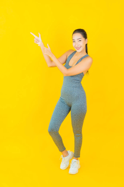 Muotokuva kaunis nuori aasialainen nainen, jolla on urheiluvaatteet valmiina liikuntaan keltaisella taustalla - Valokuva, kuva