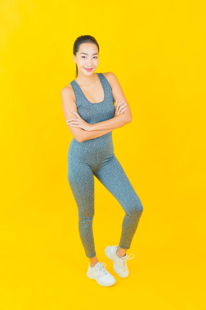 Портрет красивая молодая азиатка в спортивной одежде, готовая к упражнениям на желтом фоне - Фото, изображение