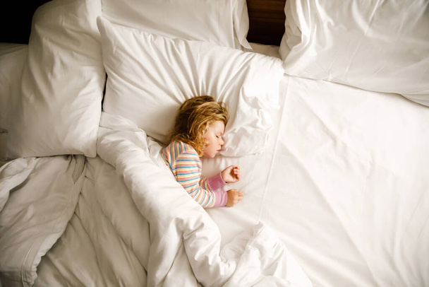 Nettes kleines Mädchen, das im großen Bett der Eltern schläft. Liebenswertes Baby träumt im Hotelbett im Familienurlaub oder zu Hause. - Foto, Bild