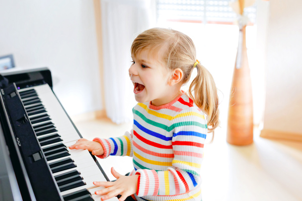 Menina pequena bonita tocando piano na sala de estar. Criança pré-escolar bonito se divertindo com a aprendizagem de tocar instrumento de música com conceito de aprendizagem durante o bloqueio do vírus corona homeschooling. - Foto, Imagem