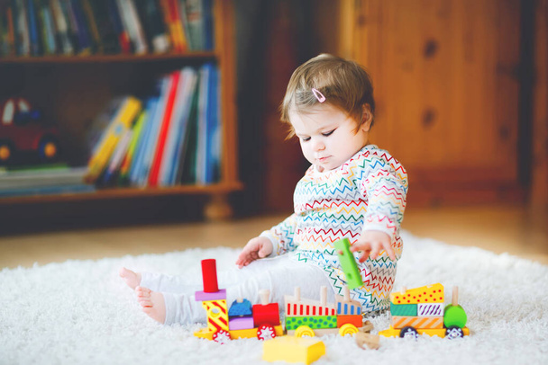 little baby girl playing with educational wooden toys at home or nursery. Toddler with colorful train. Child having fun with different toys. Lonely kid during corona virus pandemic quarantine - Photo, Image