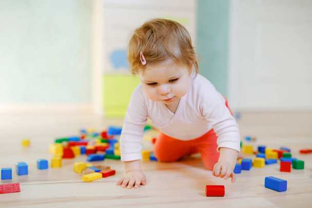 Słodka dziewczynka bawiąca się zabawkami edukacyjnymi. Szczęśliwe zdrowe dziecko bawiące się kolorowymi różnymi drewnianymi klockami w domu lub przedszkolu. Baby crawling i uczenia się kolorów i form, w pomieszczeniach - Zdjęcie, obraz