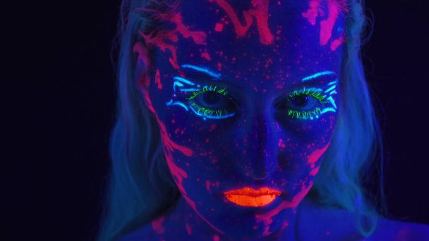 Junge Frau mit glänzendem Make-up im UV-Licht - Foto, Bild