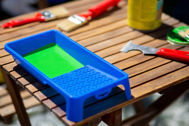 A closeup shot of a blue container with green paint on a wooden table with construction too - Fotografie, Obrázek