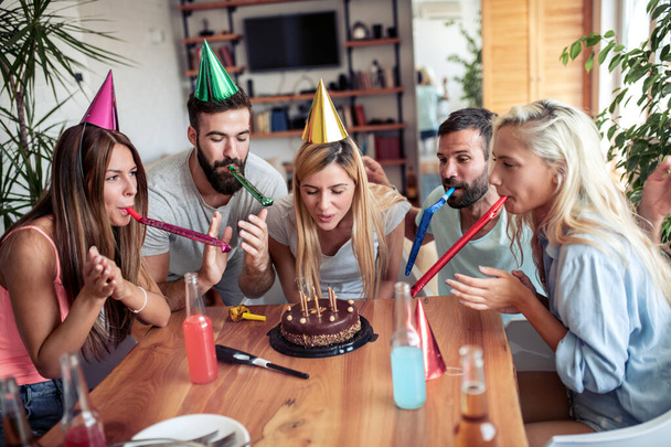 Ομάδα χαρούμενων νέων που κάνουν πάρτι γενεθλίων στο σπίτι. - Φωτογραφία, εικόνα