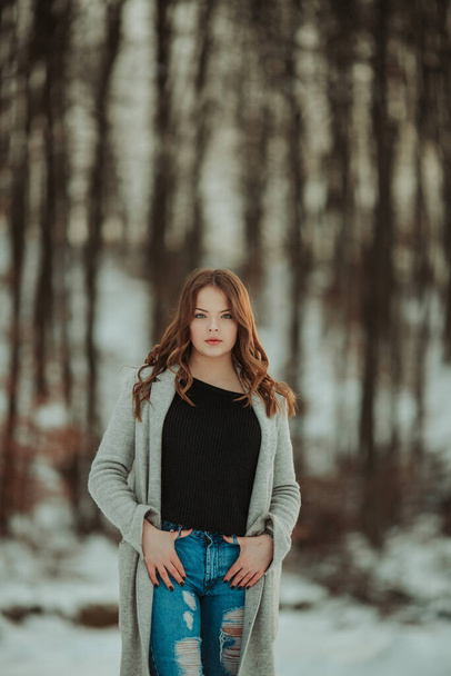 A shallow focus shot of a young Bosnian girl posing in a snowy forest wearing a gray coat and jeans - Foto, Bild