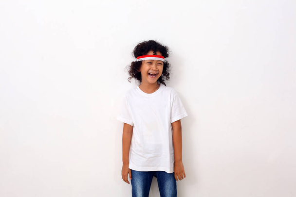 Niño asiático feliz con diadema roja blanca de pie sobre fondo blanco. - Foto, Imagen