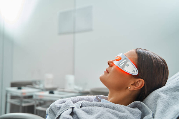 Paziente donna in occhiali sottoposta a una procedura cosmetica - Foto, immagini